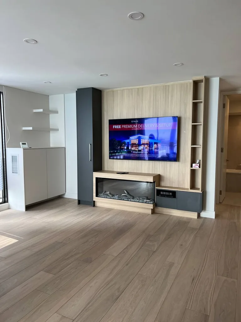Actual installation: TV above a linear fireplace on a light wood-look feature wall with surrounding storage.