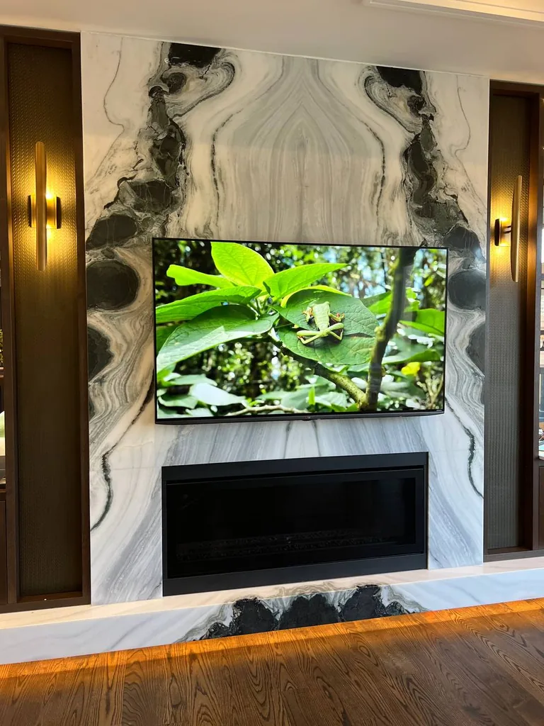 Actual installation: television mounted above a linear fireplace on a book-matched marble surround with side lighting.