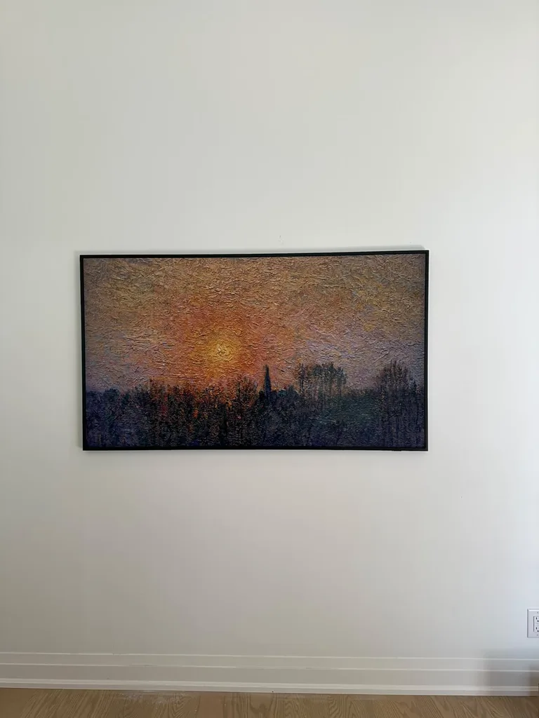 Samsung Frame TV mounted flush in a black bezel on a white wall, showing a sunset painting in Art Mode.