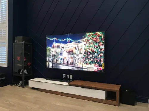 TV and soundbar mounted on a navy diagonal slat feature wall above a white and walnut console