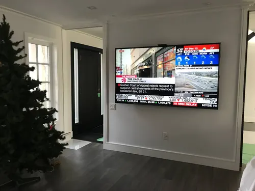 TV mounted on a white foyer wall showing a news channel, beside the front entry