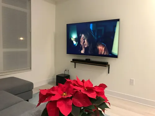TV mounted on a white condo wall above a dark floating shelf holding the AV equipment
