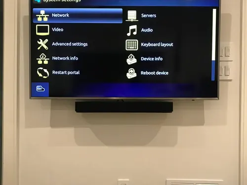 TV and soundbar mounted on a beige wall above paired outlet and low-voltage plates for the concealed cable run