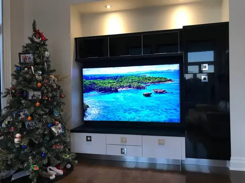 TV recessed into a black gloss built-in wall unit with upper cabinets and drawers below