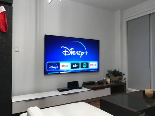 TV mounted on a white condo wall above a low white and walnut console, beside a black marble return