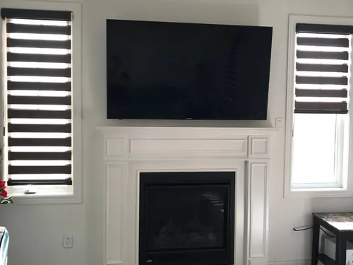 TV mounted above a traditional painted mantel and gas fireplace, between two blinded windows