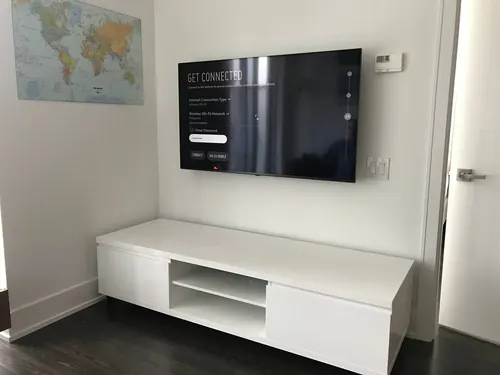 TV mounted on a white wall beside a framed world map, above a low white console
