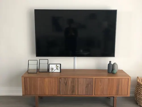 TV on a tilting mount above a walnut sideboard, with a single cable dropped to the equipment below
