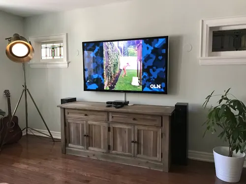 TV mounted on a pale green wall above a weathered wood sideboard, with a floor speaker alongside