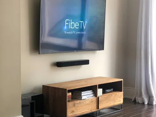 TV with a soundbar mounted on its own bracket below, above an oak console