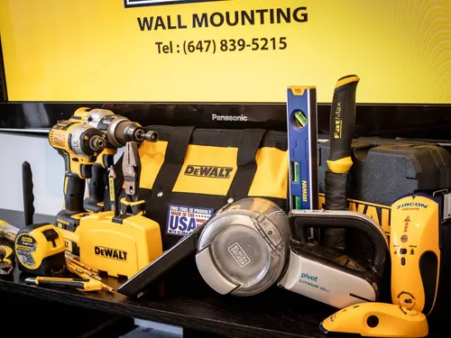 Drills, levels, a stud finder and a tool bag laid out in front of a screen showing the company logo