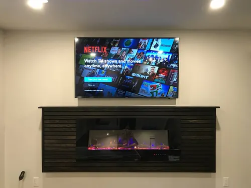 TV mounted above a dark slatted wall unit housing a linear electric fireplace in a basement