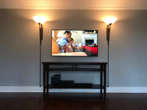 TV mounted on a grey wall between two wall-mounted swing arm lamps, above a black console table