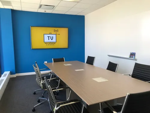 TV mounted on a blue accent wall at the head of an office boardroom
