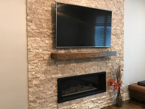 TV mounted on a travertine ledgestone chimney above a timber mantel and linear fireplace