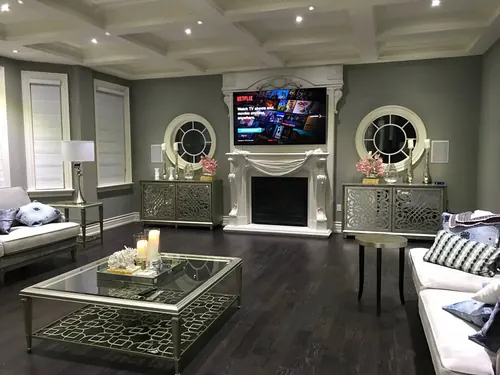 TV mounted above a carved white marble mantel in a formal living room with mirrored consoles
