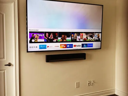 TV and soundbar mounted on a cream wall above the outlet and cable plates feeding them