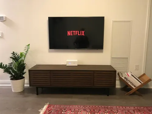 TV mounted flush on a cream wall above a slatted walnut console