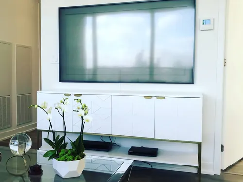 Large TV mounted on a white panel wall above a white and brass sideboard