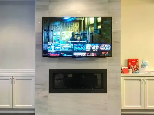 TV mounted on a marble-look porcelain chimney above a linear fireplace, between white cabinets