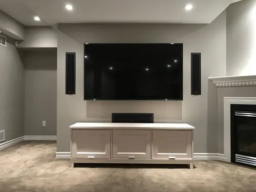 TV mounted in a basement between two wall-mounted tower speakers, with a centre speaker on the cabinet below