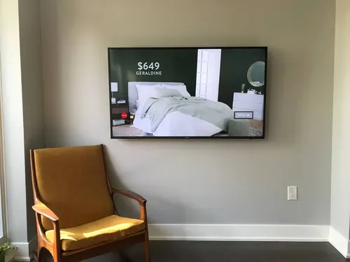 TV mounted on a showroom wall running product pricing, beside a single armchair