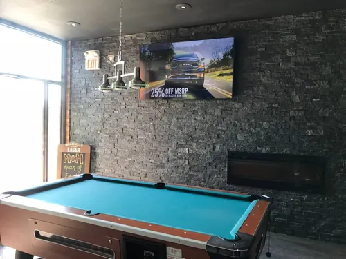 TV mounted on a stacked stone bar wall above a linear fireplace, overlooking a pool table