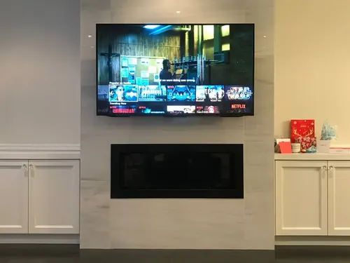 TV mounted on a porcelain slab chimney above a linear fireplace, flanked by white cabinetry