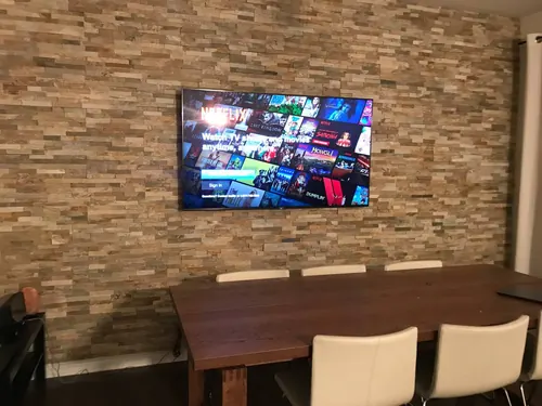 TV mounted on a reclaimed timber plank feature wall above a dining table