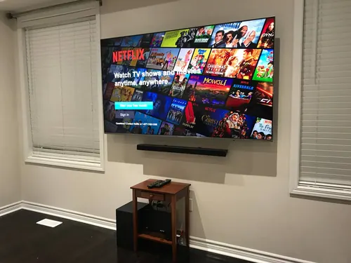 TV and soundbar mounted on a grey wall between two windows, above a small wood side table