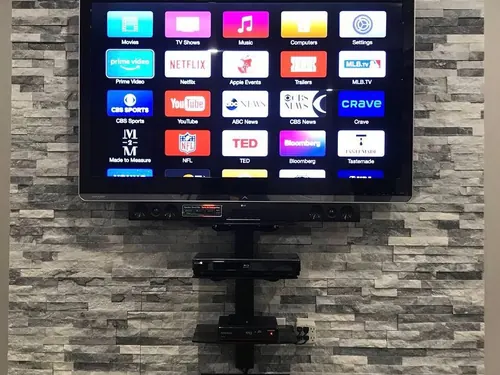 TV mounted on a stacked stone wall with the AV equipment carried on a bracket shelf and the cabling gathered below