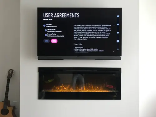 TV mounted above a wall-hung linear electric fireplace on a plain white wall