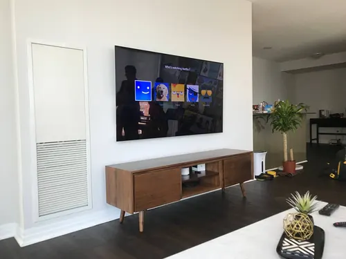 TV mounted on a white wall above a walnut mid-century console in a bright condo