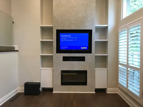TV recessed into a plaster chimney breast above a linear fireplace and a centre speaker slot, between white bookcases