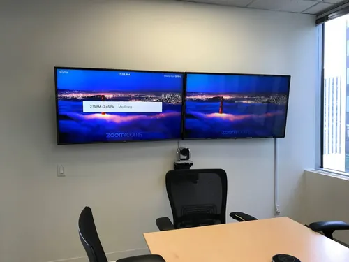 Two TVs mounted side by side in a meeting room with a conference camera fitted between them