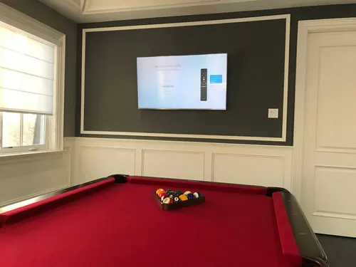 TV mounted on a dark grey panelled accent wall above wainscoting in a games room
