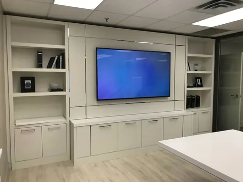 TV recessed into a white built-in office wall unit with shelving and cabinets either side
