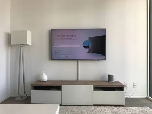 TV mounted on a white wall with the cable run enclosed in a slim white cover down to the console