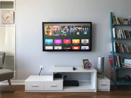 TV mounted on a pale wall above a white console, beside a blue ladder bookshelf