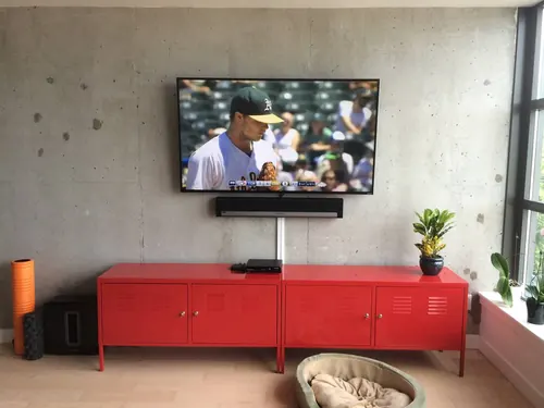 TV and soundbar mounted on a bare concrete loft wall above a red locker console