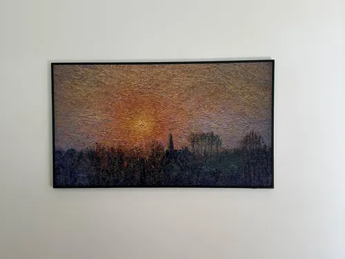 Samsung Frame TV mounted flush in a black bezel on a white wall, showing a sunset painting in Art Mode
