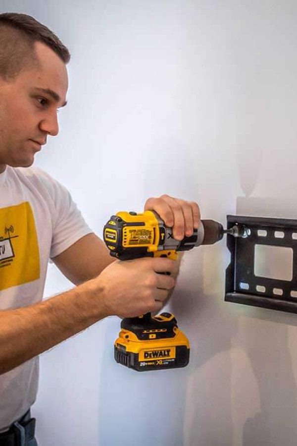 Installer levelling a TV wall mount bracket against a stud before fixing it