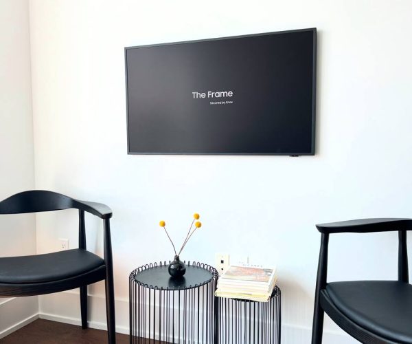 Samsung Frame TV mounted flush on a white wall above two black chairs and side tables