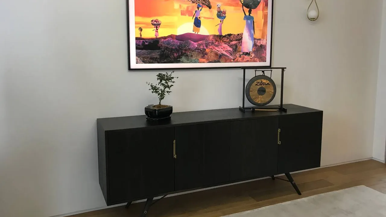 Samsung Frame TV in art mode above a black credenza, mounted flush on a plain wall