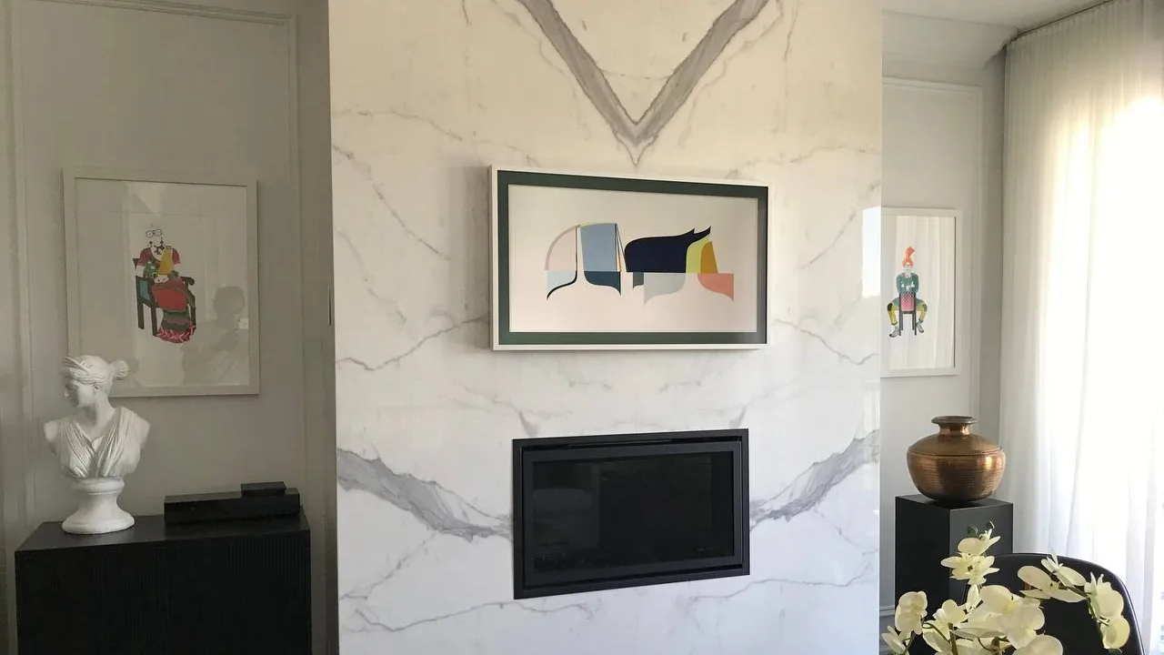 Samsung Frame TV with a white bezel mounted flush on a marble fireplace wall above a linear gas firebox