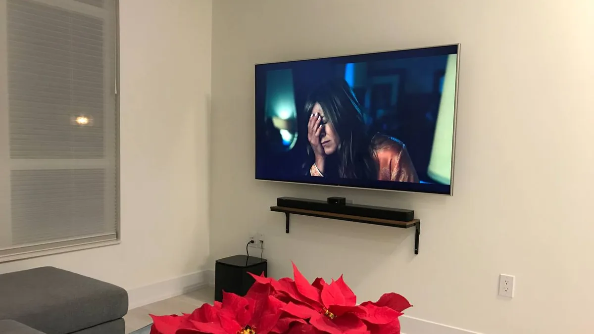Wall mounted TV with a soundbar on a slim shelf directly beneath it in a living room
