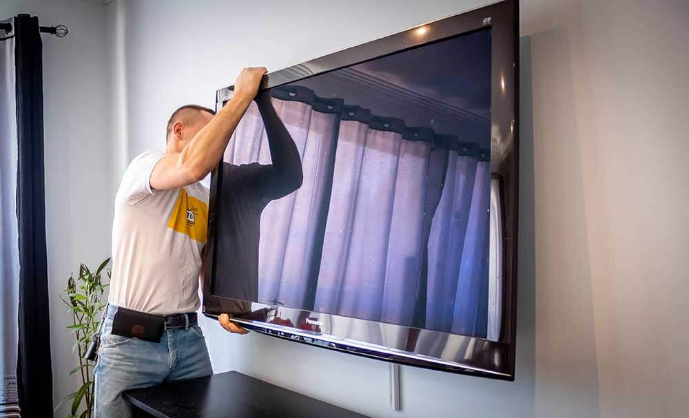 Two installers lifting a large flat-screen TV onto a wall bracket together