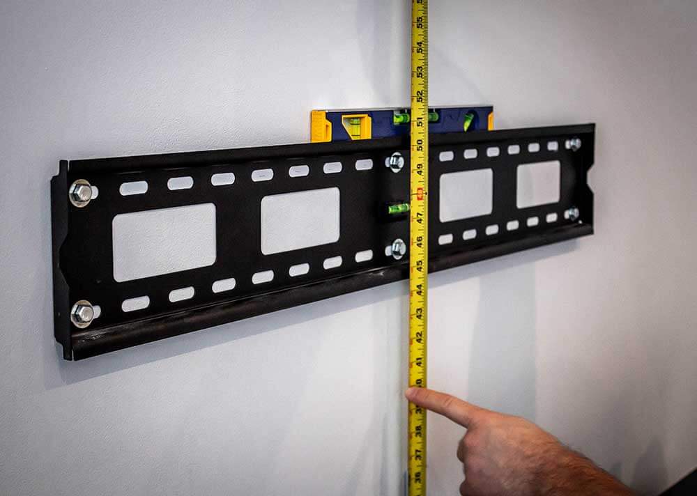 Installer measuring and marking the mounting height on a wall with a tape measure and pencil