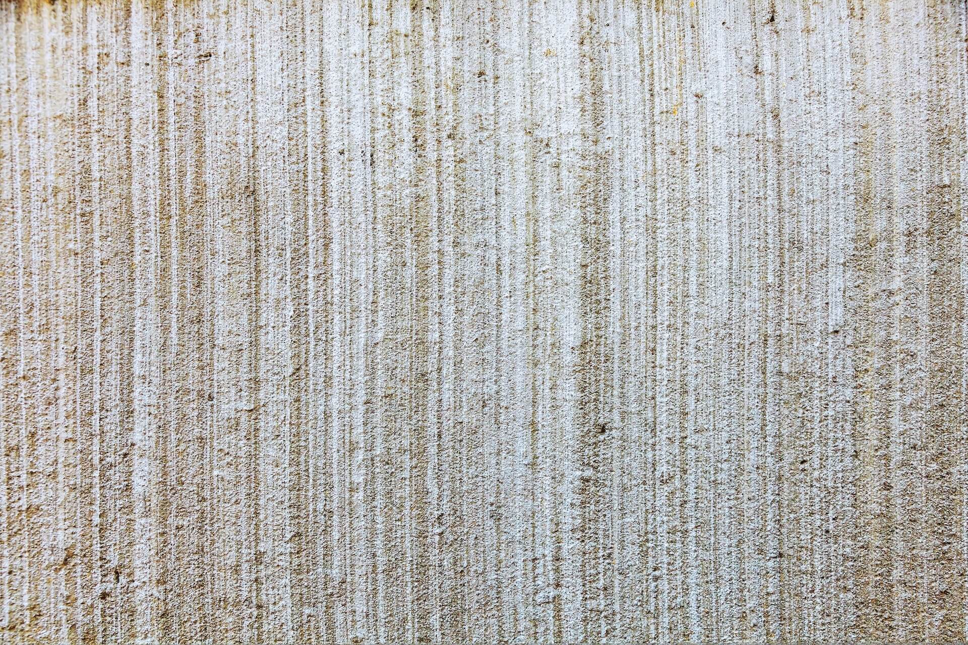 Close-up of a textured wall surface with vertical lines, perfect for TV wall mounting. The wall appears to be painted in a light beige color with a rough, gritty finish. The lines create a pattern throughout the surface, offering a sense of depth and structure.
