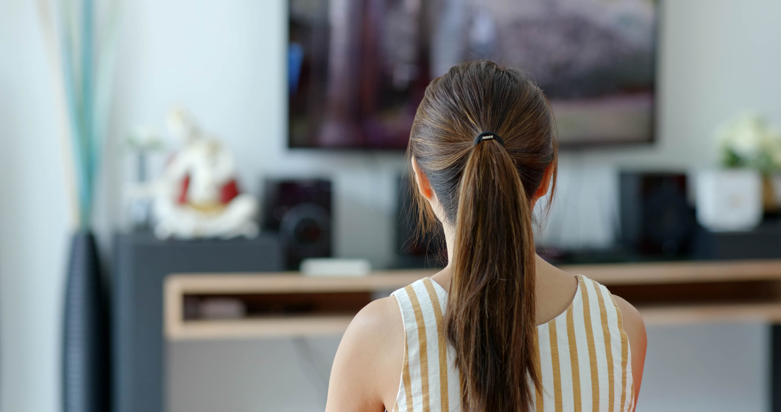 A person standing and watching a wall-mounted TV, showing the raised sight line a home gym screen has to serve